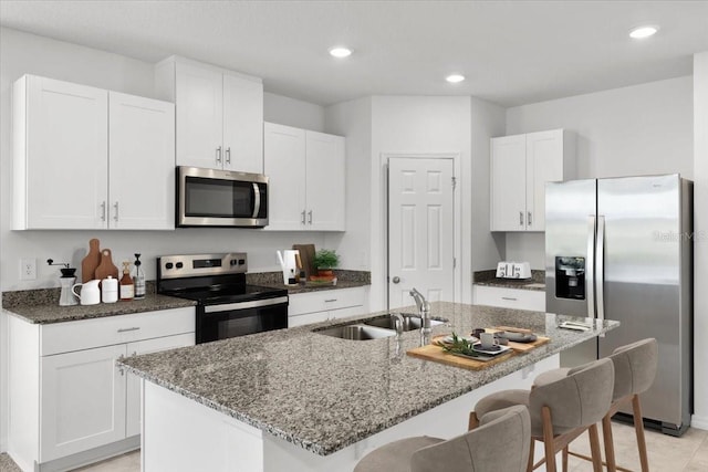 kitchen with sink, a kitchen island with sink, stainless steel appliances, and white cabinets