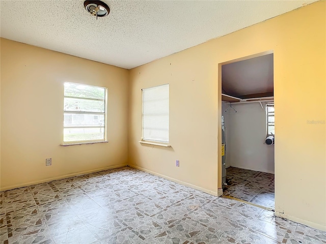 unfurnished bedroom featuring a spacious closet, a textured ceiling, a closet, and light tile flooring