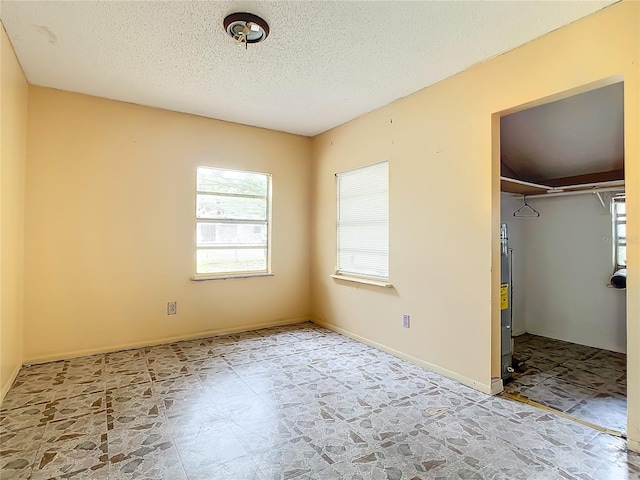 unfurnished bedroom featuring a closet, a textured ceiling, light tile flooring, and water heater