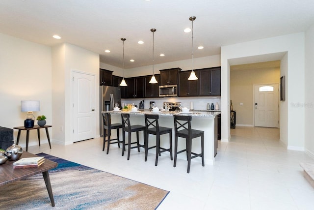 kitchen featuring an island with sink, pendant lighting, light stone counters, a kitchen bar, and appliances with stainless steel finishes