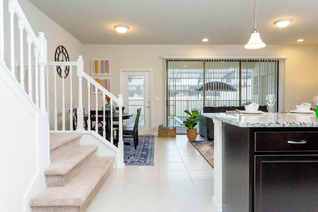 kitchen featuring light stone counters, dark brown cabinetry, light tile floors, and pendant lighting