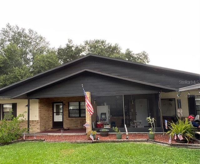 rear view of house featuring a sunroom, a yard, and brick siding