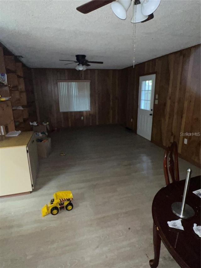 interior space featuring light wood-type flooring, wood walls, ceiling fan, and a textured ceiling