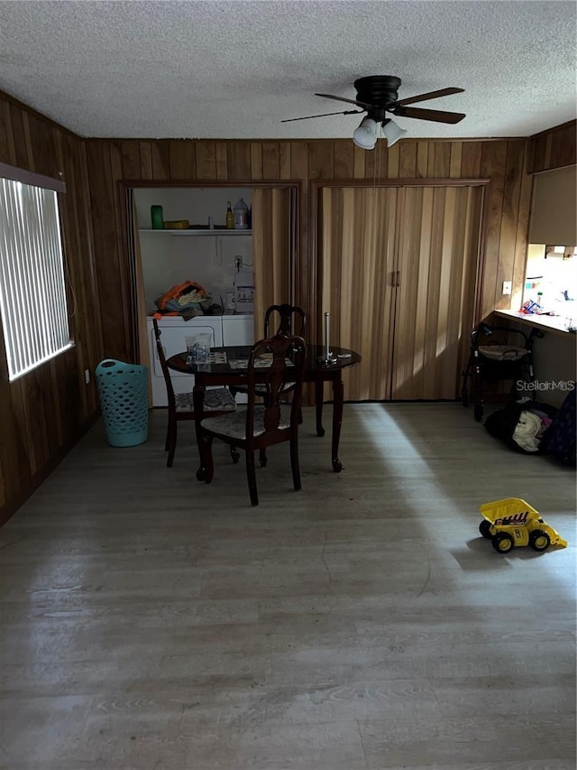 unfurnished dining area featuring light wood-style floors, ceiling fan, wooden walls, and a textured ceiling