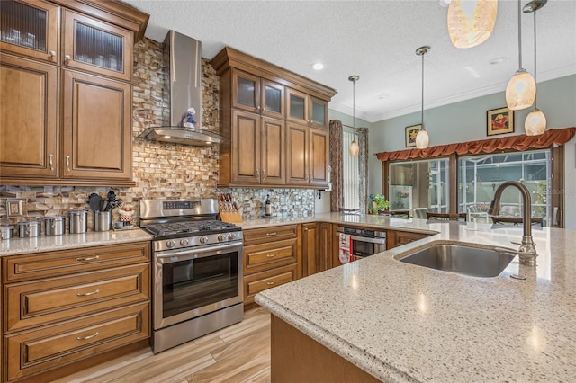 kitchen with light stone counters, backsplash, wall chimney exhaust hood, stainless steel range with gas cooktop, and sink