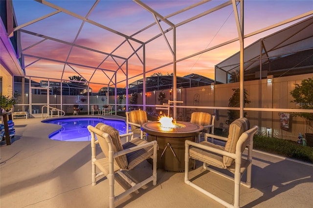 pool at dusk featuring a fire pit, glass enclosure, and a patio area