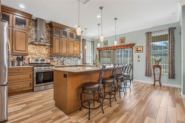 kitchen featuring wall chimney exhaust hood, light hardwood / wood-style floors, stainless steel appliances, and backsplash