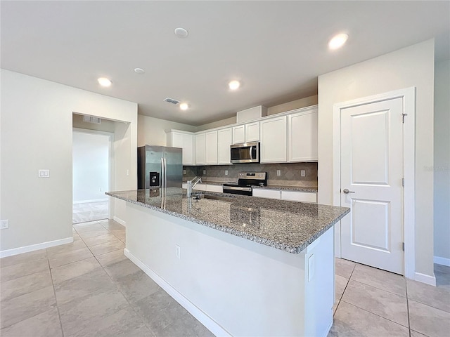 kitchen with dark stone counters, stainless steel appliances, sink, a center island with sink, and white cabinets