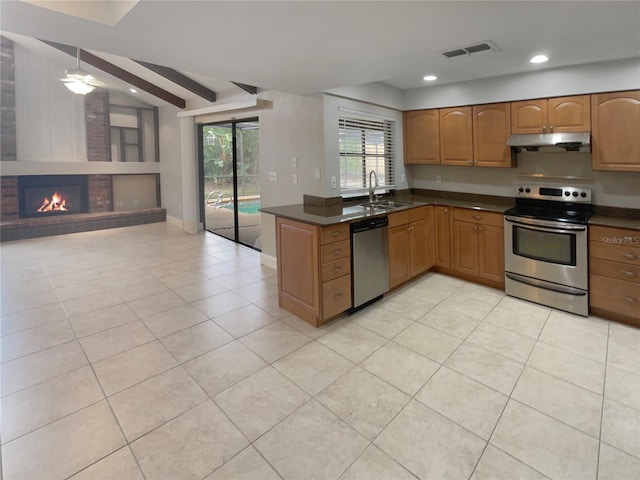 kitchen with sink, a brick fireplace, ceiling fan, light tile patterned floors, and stainless steel appliances