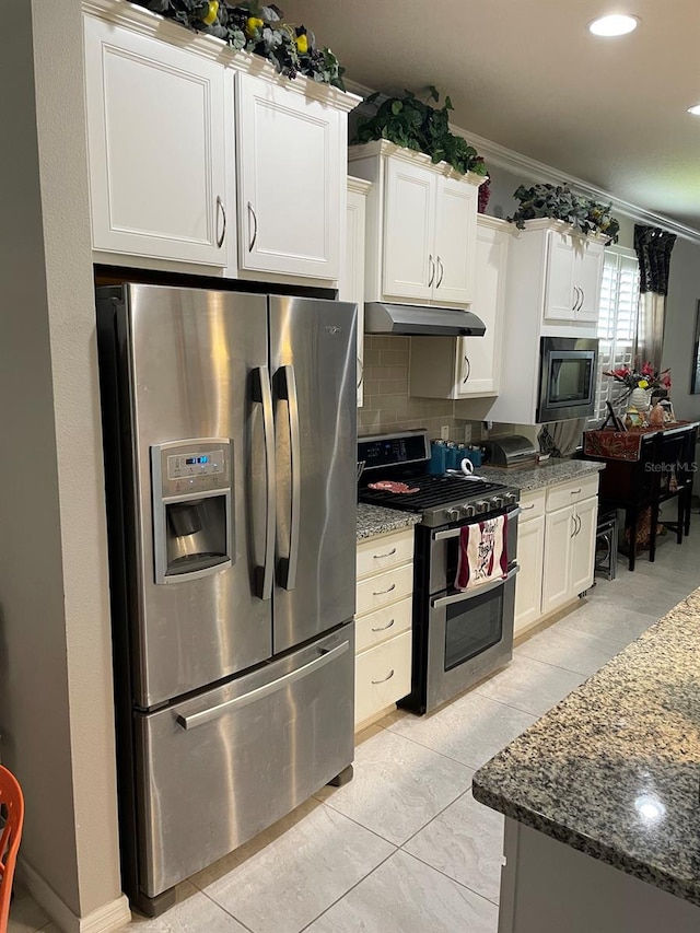 kitchen featuring dark stone countertops, white cabinetry, stainless steel appliances, and ornamental molding