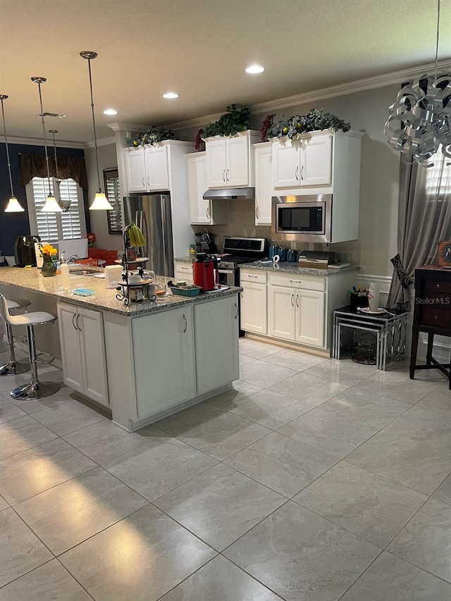 kitchen with hanging light fixtures, white cabinets, stainless steel appliances, and ornamental molding