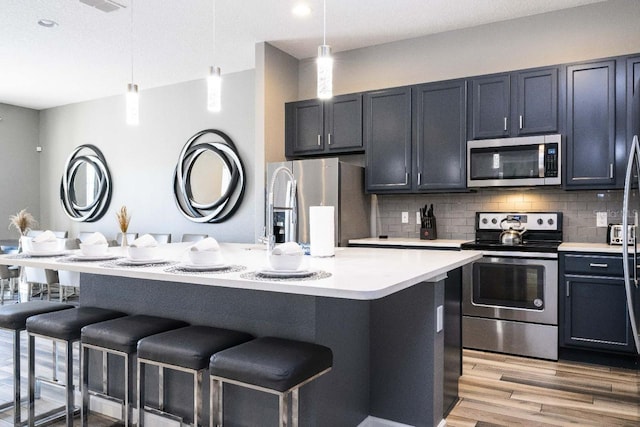 kitchen with appliances with stainless steel finishes, tasteful backsplash, light wood-type flooring, and pendant lighting