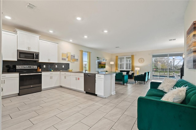 kitchen featuring tasteful backsplash, kitchen peninsula, white cabinetry, and appliances with stainless steel finishes