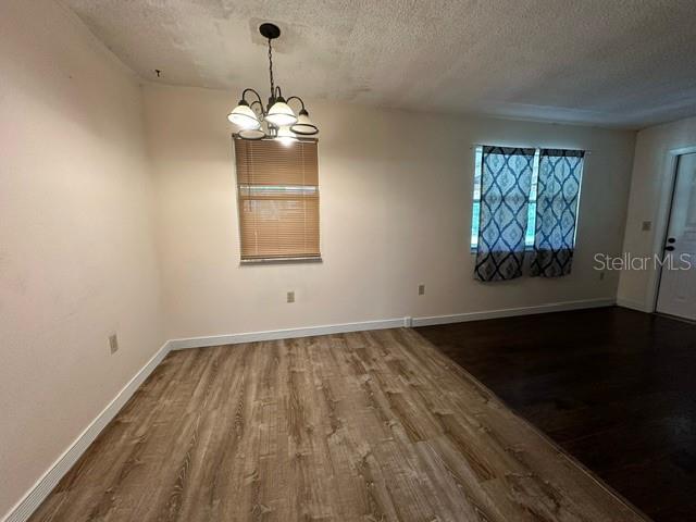 unfurnished room featuring a textured ceiling, a notable chandelier, and hardwood / wood-style floors