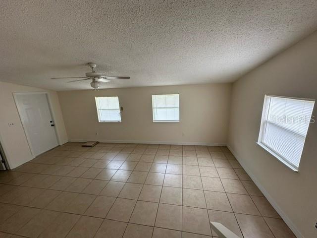 unfurnished room with ceiling fan, a textured ceiling, and light tile floors