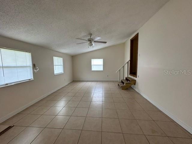 empty room with light tile floors, a textured ceiling, ceiling fan, and vaulted ceiling