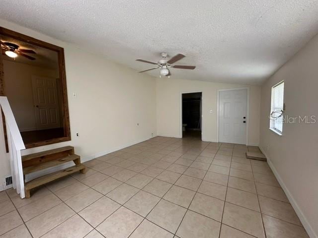 unfurnished room with a textured ceiling, ceiling fan, light tile floors, and lofted ceiling