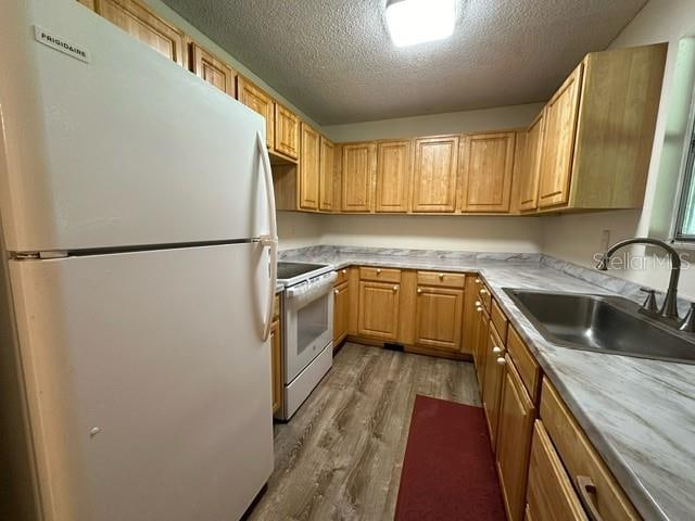 kitchen featuring a textured ceiling, white appliances, wood-type flooring, sink, and light brown cabinetry