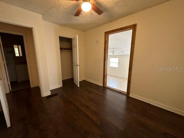 unfurnished bedroom featuring ceiling fan, a closet, a textured ceiling, and dark wood-type flooring