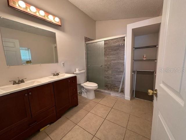 bathroom with walk in shower, tile flooring, a textured ceiling, double sink vanity, and toilet