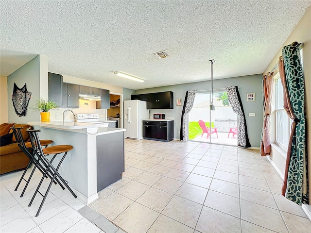 kitchen with light tile patterned flooring, a kitchen breakfast bar, gray cabinets, kitchen peninsula, and white appliances