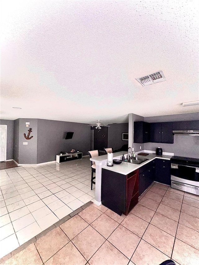 kitchen with sink, light tile patterned floors, a textured ceiling, and stainless steel range oven