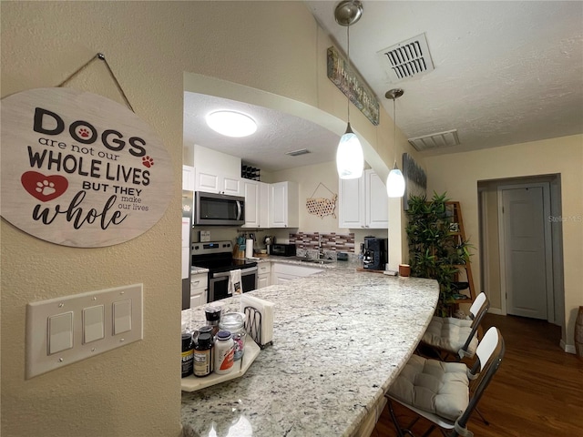 kitchen featuring dark hardwood / wood-style flooring, white cabinetry, appliances with stainless steel finishes, sink, and pendant lighting