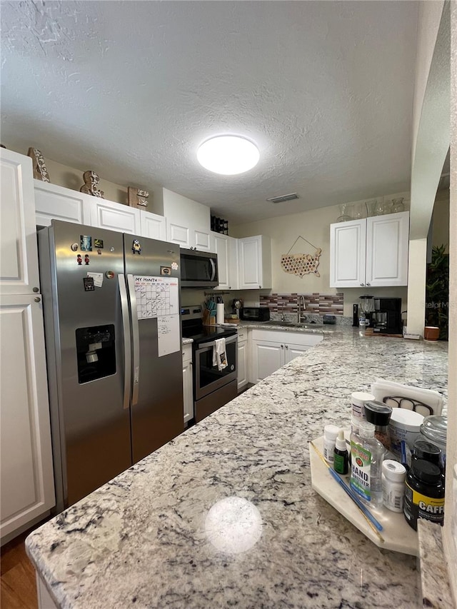 kitchen featuring light stone countertops, appliances with stainless steel finishes, white cabinets, hardwood / wood-style floors, and sink