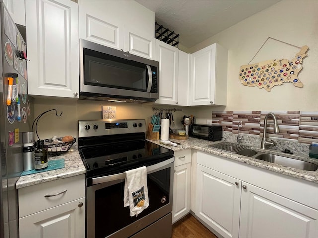 kitchen with dark hardwood / wood-style floors, light stone counters, sink, white cabinetry, and appliances with stainless steel finishes