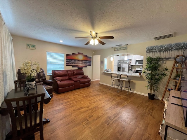 living room featuring a textured ceiling, wood-type flooring, and ceiling fan