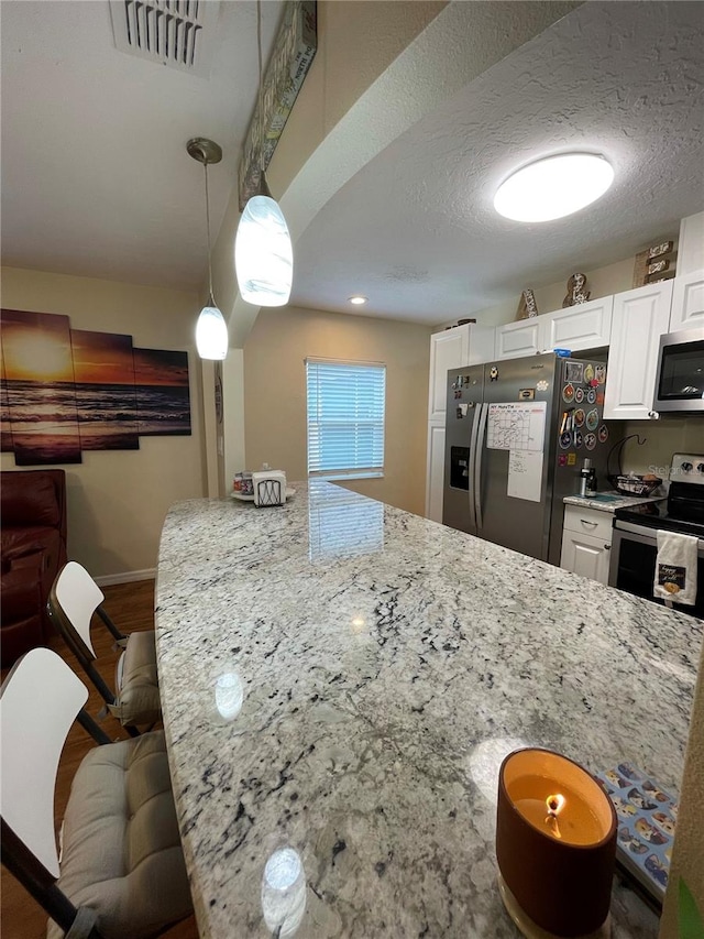 kitchen with a kitchen breakfast bar, decorative light fixtures, light stone counters, white cabinetry, and appliances with stainless steel finishes