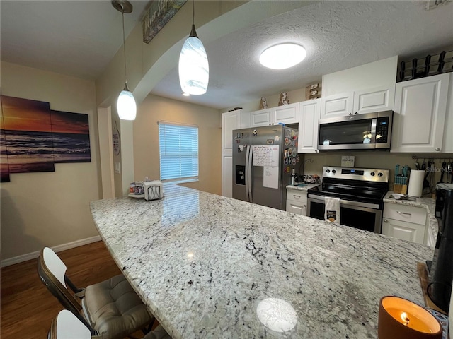 kitchen with a kitchen breakfast bar, light stone countertops, wood-type flooring, appliances with stainless steel finishes, and pendant lighting