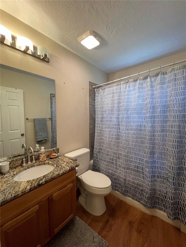 bathroom with wood-type flooring, vanity with extensive cabinet space, toilet, and a textured ceiling