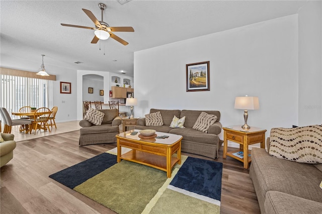 living room with a textured ceiling, wood-type flooring, and ceiling fan