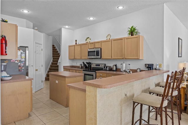 kitchen featuring appliances with stainless steel finishes, a textured ceiling, light tile floors, and kitchen peninsula