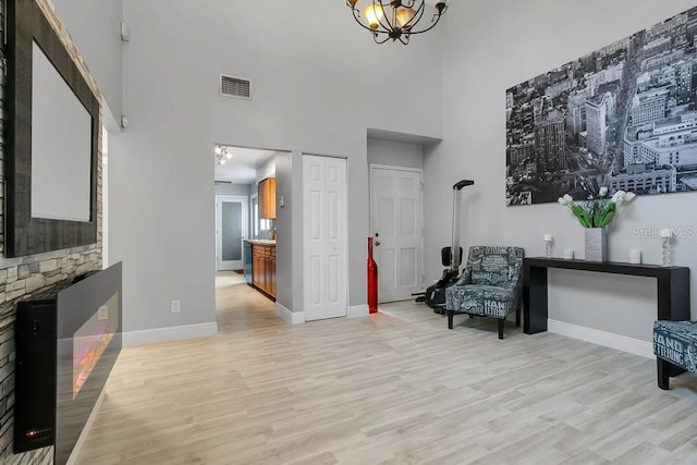 living area featuring light wood-type flooring, visible vents, a towering ceiling, and baseboards