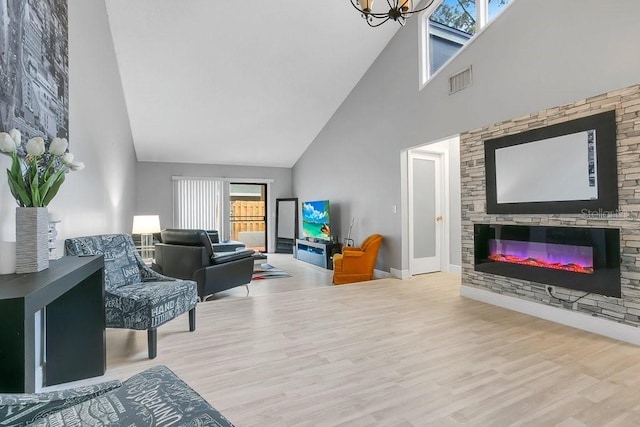 living area featuring a glass covered fireplace, a high ceiling, wood finished floors, and visible vents