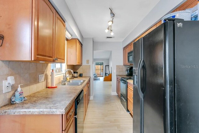 kitchen with a sink, light countertops, light wood-type flooring, black appliances, and tasteful backsplash