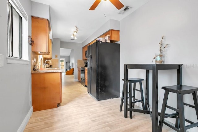 kitchen with brown cabinetry, a sink, light wood finished floors, and black appliances