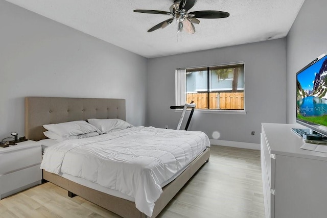 bedroom with baseboards, ceiling fan, a textured ceiling, and light wood-style floors