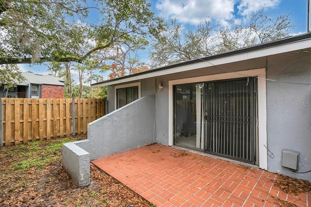 view of exterior entry featuring a patio area, fence, and stucco siding