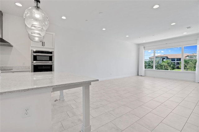 kitchen featuring light stone counters, light tile floors, wall chimney exhaust hood, stainless steel double oven, and white cabinetry