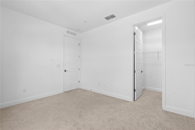 unfurnished bedroom with a closet, light carpet, and a spacious closet