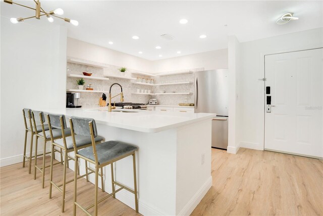 kitchen featuring white cabinets, kitchen peninsula, sink, light wood-type flooring, and stainless steel fridge