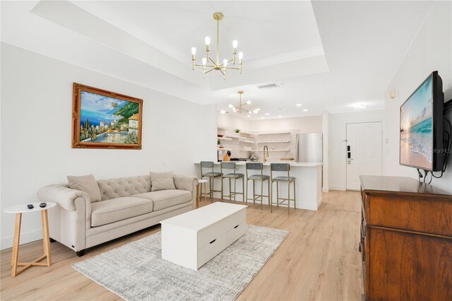 living room with light hardwood / wood-style floors, a notable chandelier, sink, and a raised ceiling