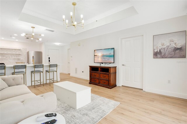 living room with light hardwood / wood-style floors, a notable chandelier, and a tray ceiling