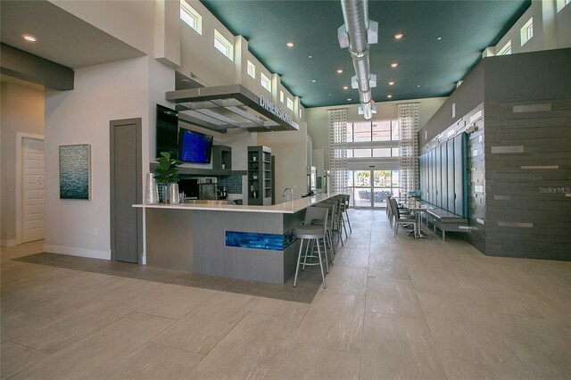 kitchen featuring a kitchen breakfast bar, a towering ceiling, light tile patterned flooring, and kitchen peninsula