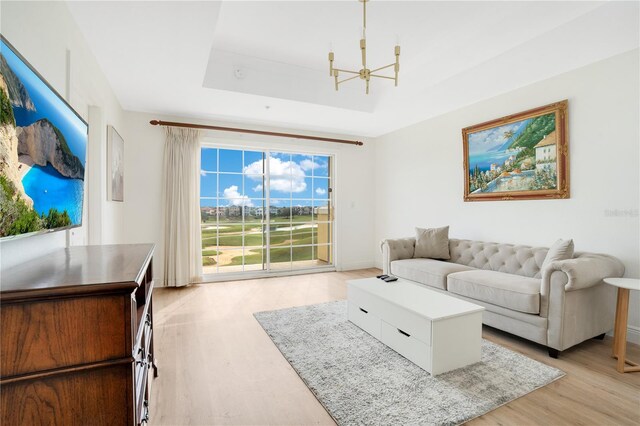 living room with light hardwood / wood-style flooring, a tray ceiling, and an inviting chandelier