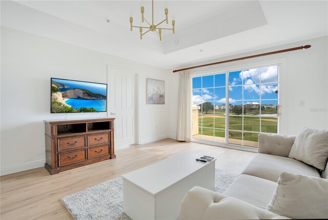 living room featuring light hardwood / wood-style floors, a raised ceiling, and an inviting chandelier