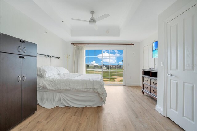 bedroom with ceiling fan, a raised ceiling, light wood-type flooring, and access to exterior